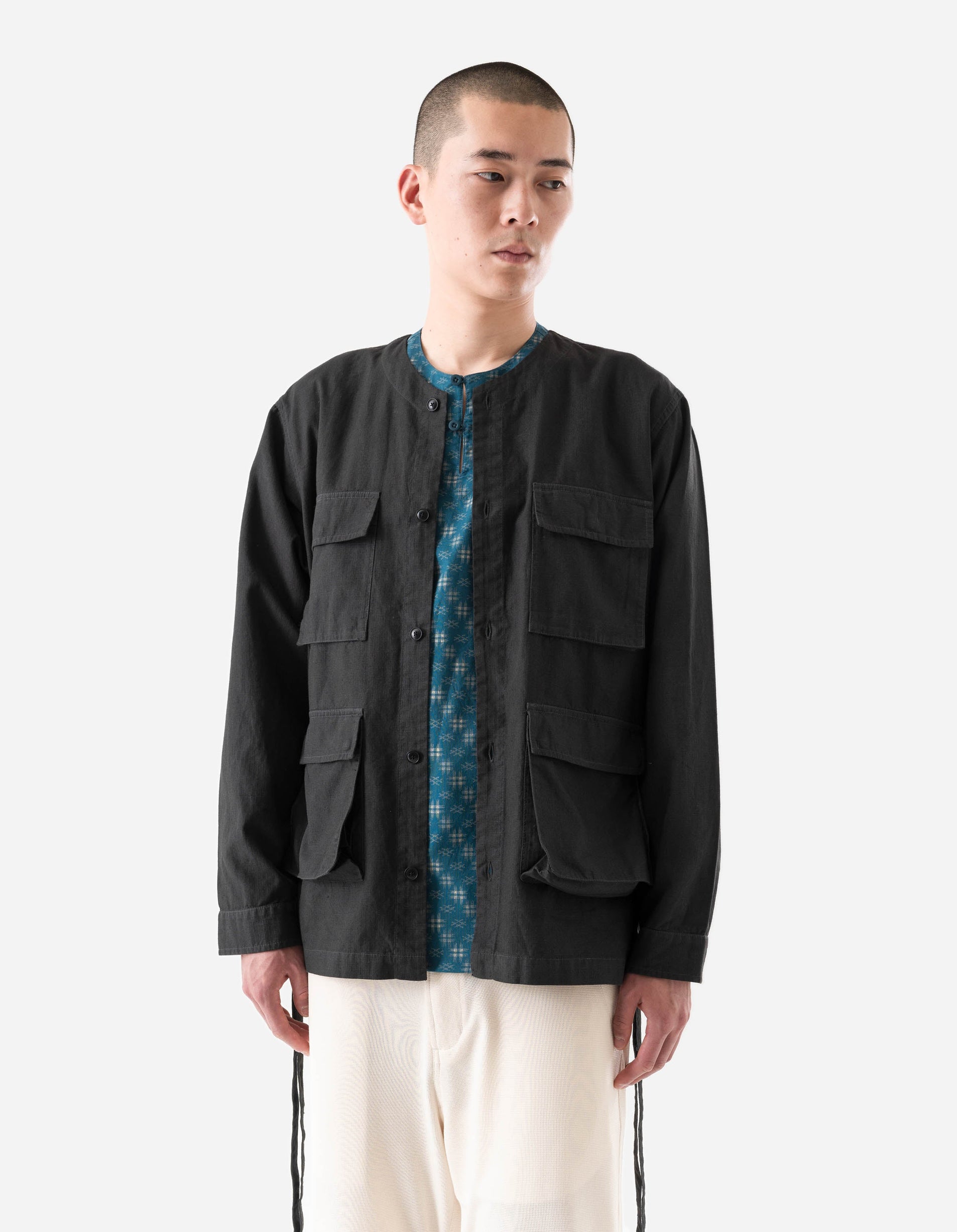 Man wearing a black jacket over a patterned shirt on a white background