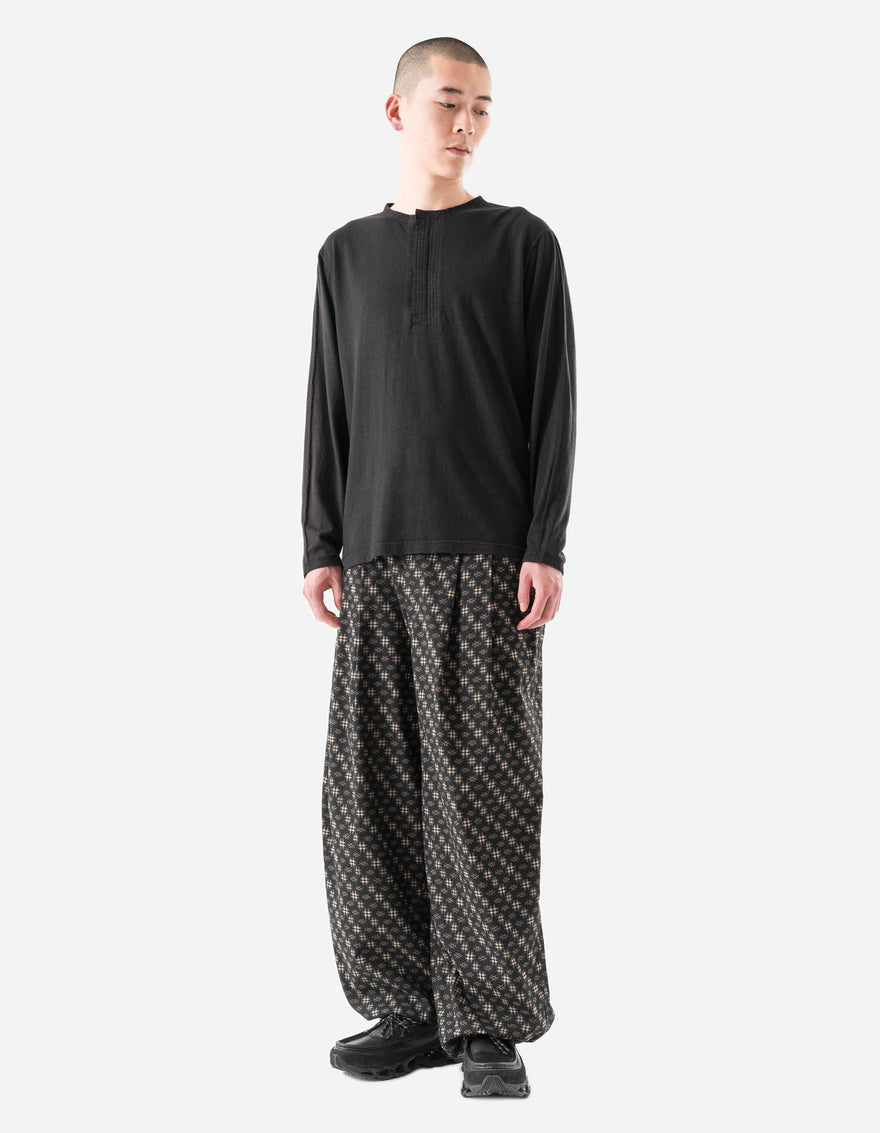 Person wearing a black long-sleeve shirt and patterned pants on a white background